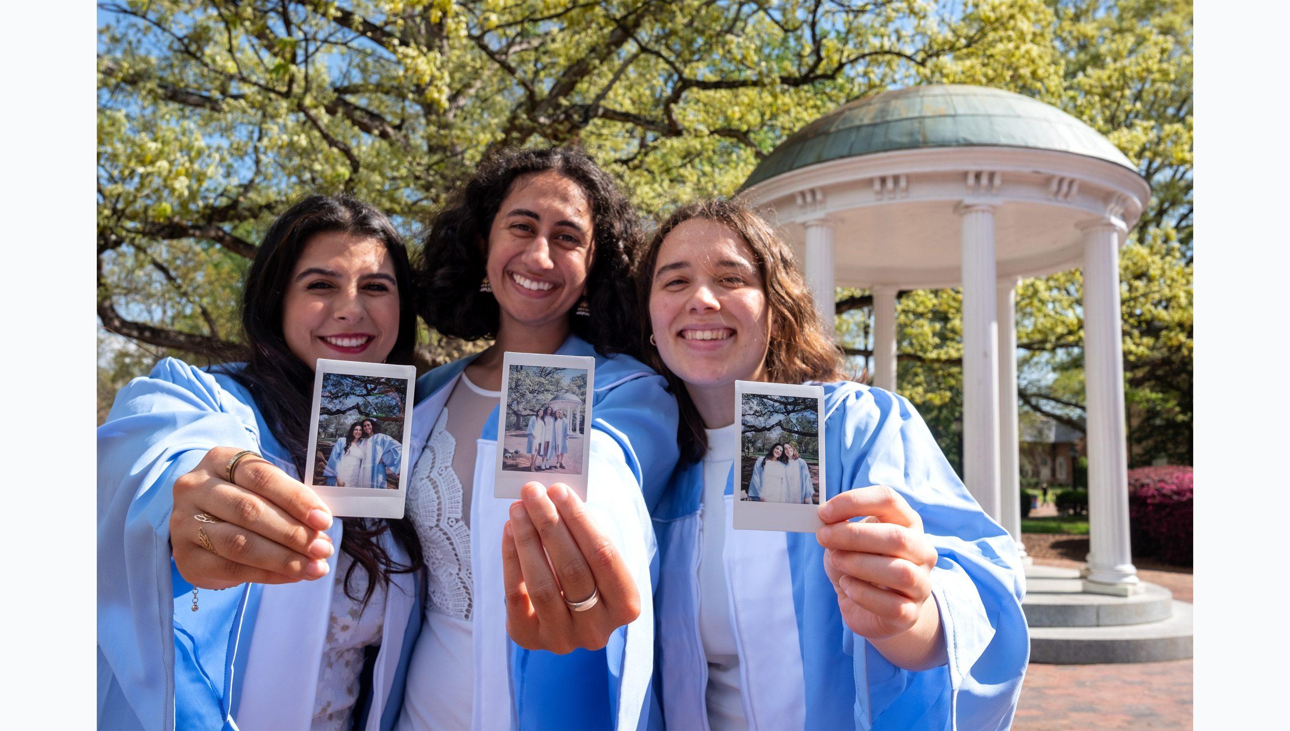 Three students holding up film photos of themselves in caps and gowns.